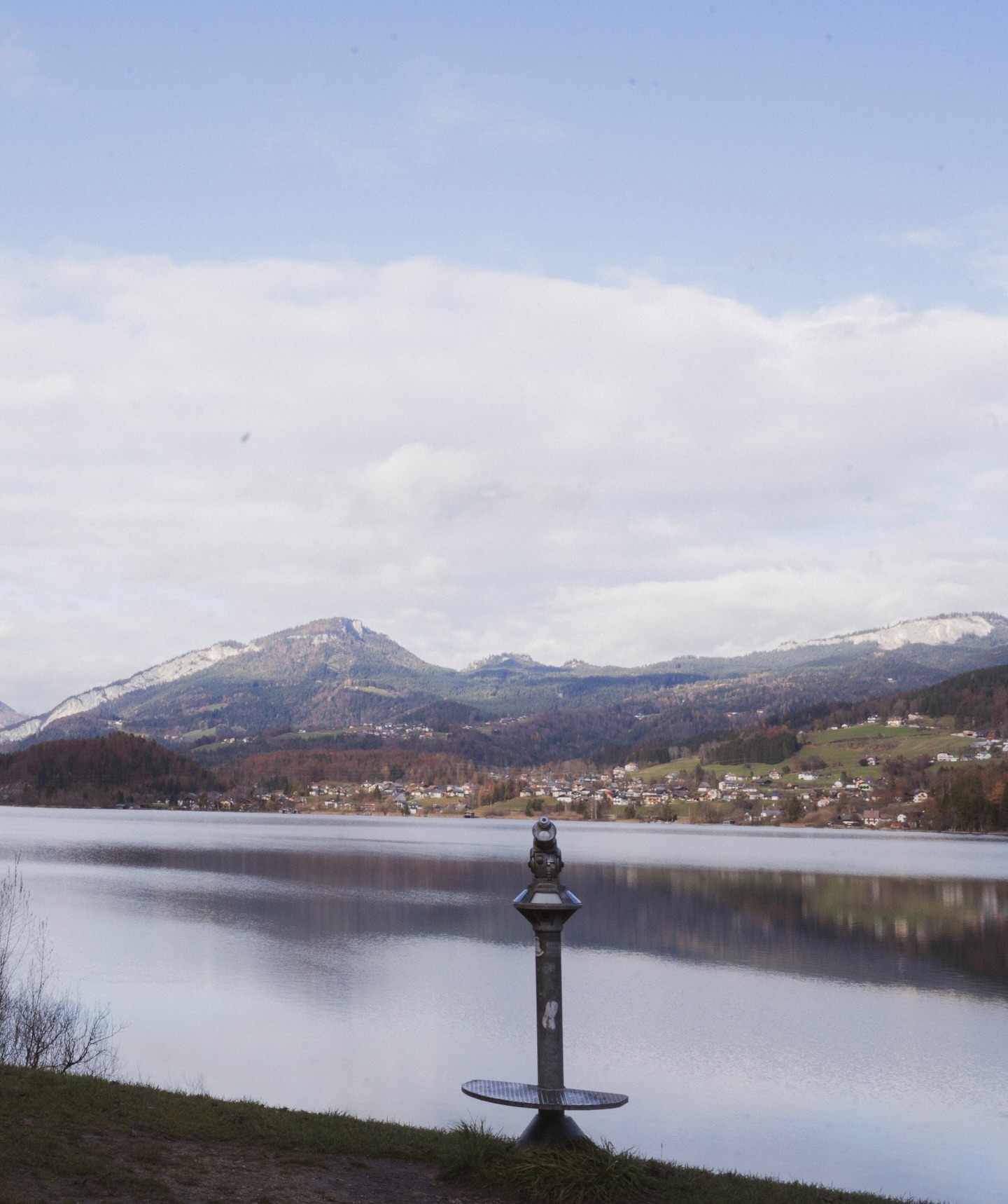 Alpine village beside a lake with an ochre forest hanging from the mountain at dawn.